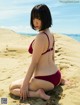 A woman in a red bikini sitting on a sandy beach.