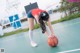 A woman bending over to pick up a basketball on a court.