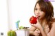 A woman sitting at a table eating a red pepper.