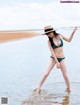 A woman in a bikini and hat standing in the water.