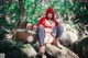 A woman in a red hooded outfit sitting on a rock with a basket.