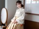 A woman in a white and gold hanbok sitting on a chair.